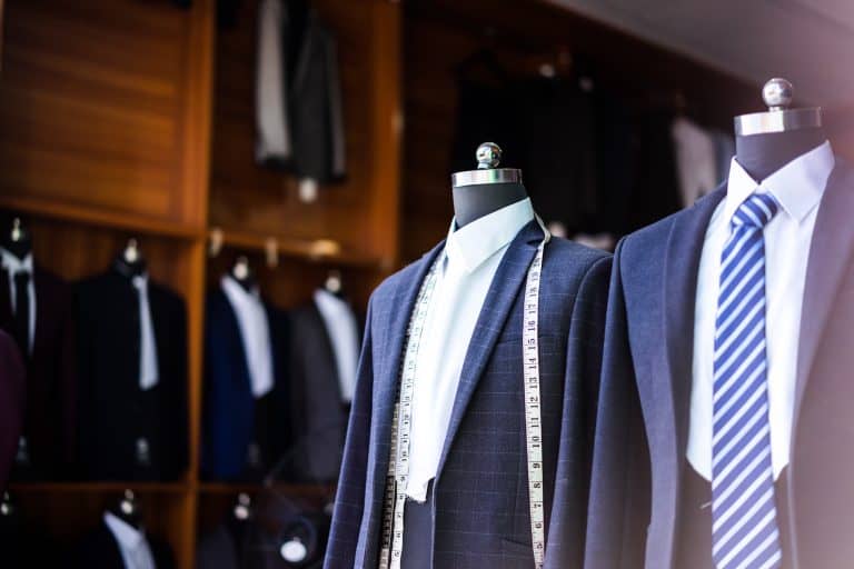 Tailored suits displayed on mannequins in a clothing showroom, with measuring tape draped over one jacket.