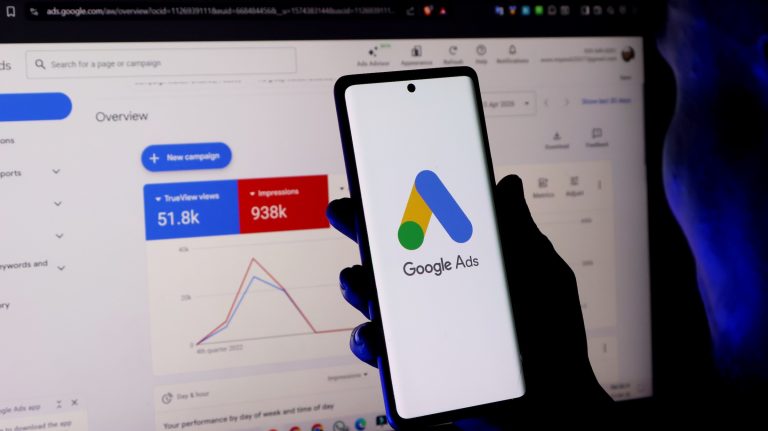 Phone showing the Google Ads logo in front of a Google Ads dashboard, representing tracking, measurement and campaign performance.