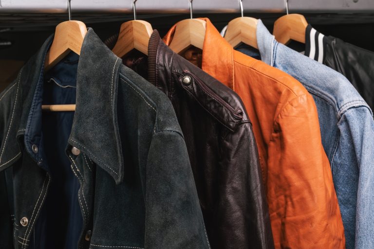 Clothing jackets hanging on wooden hangers, including leather, suede and denim outerwear.